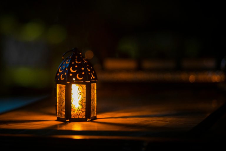 A lit lantern with geometric patterns sits on a wooden table in the dark.